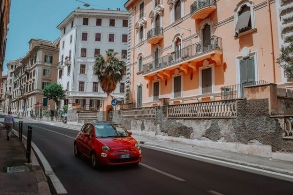 A comprehensive guide to driving in Europe. A small red car driving in a European city. Total Travel Protection.