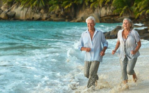 Medical travel insurance - travel insurance over 70 - mature couple running on beach